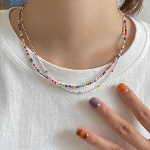 Close-up of a double-layered silver chain and colorful beaded necklace on a model