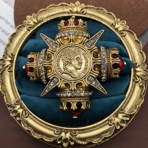 Macro shot of gold cross brooch with Napoleon relief and red gemstone details