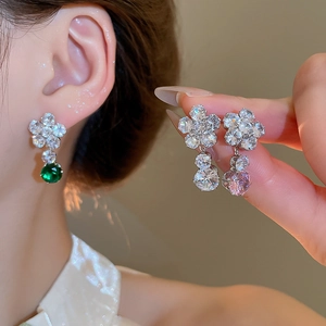 Detail of flower-shaped silver earrings with sparkling zircon and green and pink gemstones