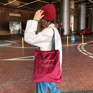 Detail of burgundy velvet tote bag featuring golden Love rewards the brave embroidery