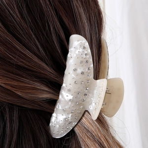 Detail of a pearl white acetate hair claw clip with rhinestones worn on brown hair
