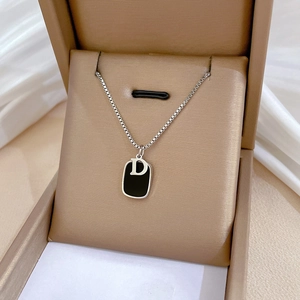 Macro view of a black geometric square pendant with silver letter D on silk fabric