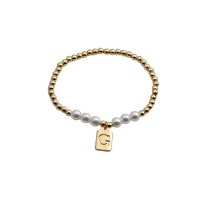 Detail view of pearl and gold bead bracelet featuring an engraved G letter pendant