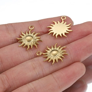 Three golden sun-shaped stainless steel charms displayed on a fingertip for size scale