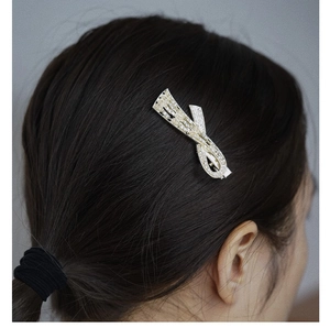 Detail of a golden bow hair clip with crystals and pearls worn by a model