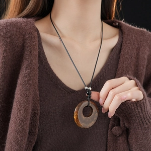 Detail of a brown resin circle pendant on a black leather cord necklace with metallic beads