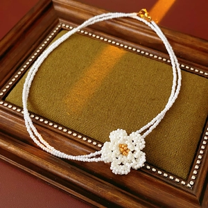 Detailed macro of white camellia beaded double-layer necklace with golden center on green fabric