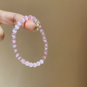Close-up of pink cat eye stone beads on a delicate bracelet with a metallic charm