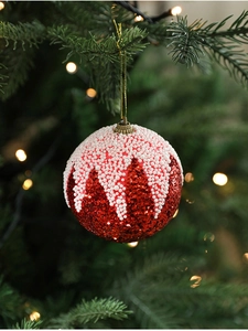 Boule de Noël rouge avec effet neige suspendue sur une branche de sapin verte décorée
