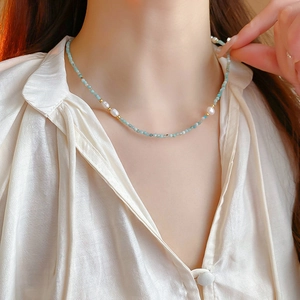 Detail of beaded necklace with turquoise beads, white pearls, and gold accents on model