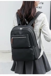 Back view of a casual black nylon backpack featuring silver zippers and brown pull tabs