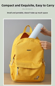 Detail showing a blue cylindrical pencil box being placed inside a yellow Snoopy canvas bag
