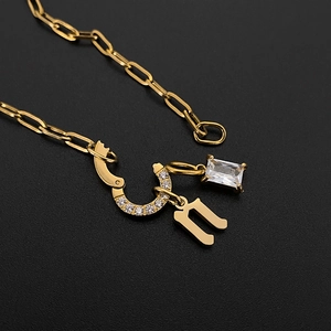 Detail of gold titanium steel necklace with initial n and horseshoe CZ charm.
