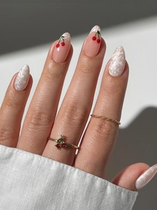Detailed view of long almond press-on nails with white texture and red cherry patterns