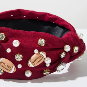 Detailed close-up of burgundy knotted headband with rhinestone football and pearl charms