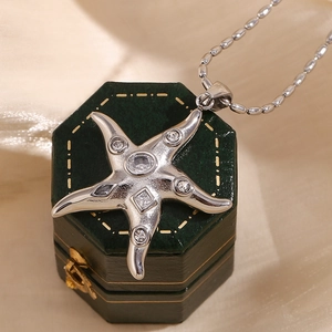Macro detail of a silver starfish pendant featuring sparkling zircon stones on green box