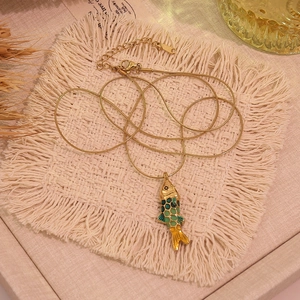 Détail d'un pendentif carpe koi dorée avec émail turquoise sur une chaîne serpent fine