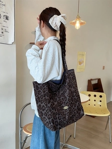 Large capacity leopard print tote bag with metal logo, worn by model in a cafe setting