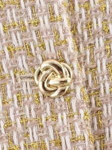 Detailed macro view of beige tweed fabric with gold thread and a metallic knot button
