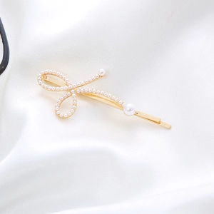 Elegant gold bow hair clip with white pearls on a soft white satin background