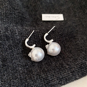 Detailed shot of C-shaped pearl earrings with silver star inlays on dark knit fabric