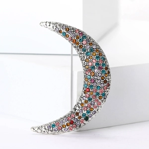 Macro shot of a crescent moon brooch with colorful rhinestones on a white pedestal