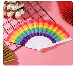 Close-up of rainbow folding fan with white plastic ribs on a pink floral background