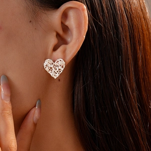 Close-up of heart-shaped silver stud earring with intricate hollow lace metal texture