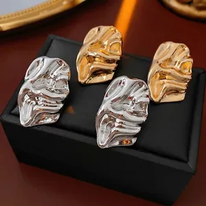 Irregular textured metal stud earrings in gold and silver finish on luxury jewelry box