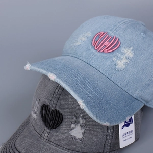 Detail of ripped denim baseball cap showing heart letters embroidery and distressed finish