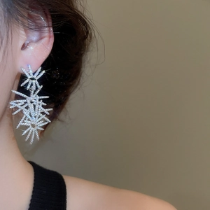 Detailed view of silver starburst drop earrings with sparkling crystals on model
