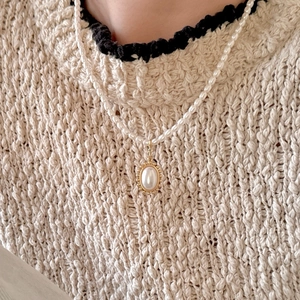 Close-up of pearl necklace with oval pendant worn on a beige knit sweater for a vintage look