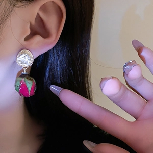 Détail de boucles d'oreilles rose avec pétales rouges et finition dorée sur un mannequin