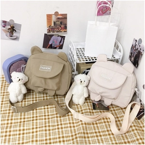 Detail of cute cat-ear canvas bags in khaki and cream with plush bear pendants