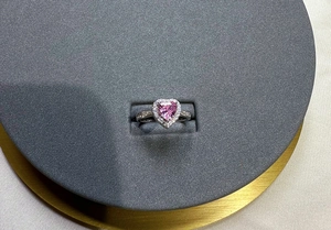 Macro detail of heart-shaped pink gem ring with halo diamonds and silver band