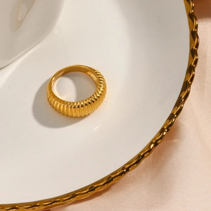 Detailed view of an 18K gold-plated ribbed ring on a pink silk fabric and white plate
