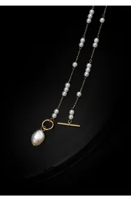 Detailed macro view of a baroque pearl pendant and golden T-clasp on long necklace