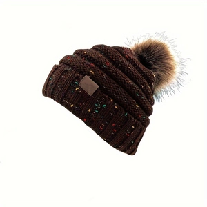 Détail d'un bonnet en maille épaisse avec mouchetures colorées, pompon et patch
