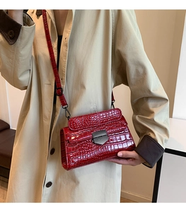 Detail of red crocodile pattern patent leather shoulder bag with dark metal buckle