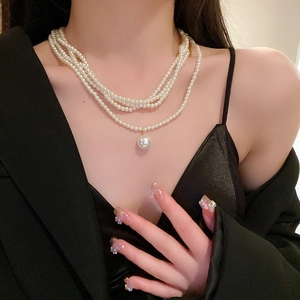 Detail of multi-layer pearl necklace with elegant large pearl pendant on black dress