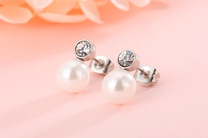 Close-up of pearl and rhinestone stud earrings on soft pink floral background