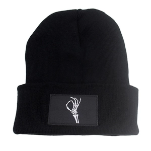 Black knit beanie featuring a white skeletal hand OK sign embroidery patch