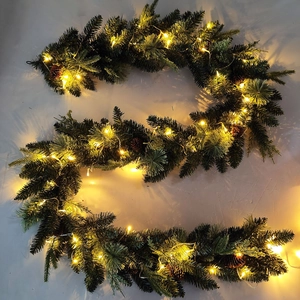 Artificial Christmas garland with pine needles, cones and warm LED lights on a gray surface