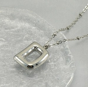 Macro detail of balloon-style silver D letter pendant with textured metal and bead chain