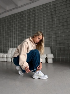 Détail d'un sweat à col zippé en polaire beige avec jogging bleu et baskets argentées