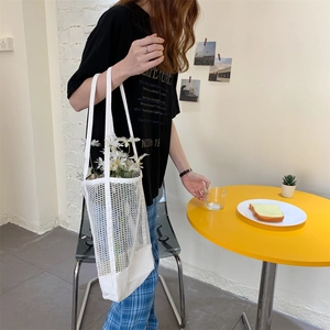 Detail of white mesh canvas tote bag with floral accents in a bright cafe setting