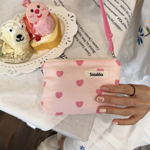 Close-up of a pink heart-patterned canvas pouch held over a sweet lifestyle background