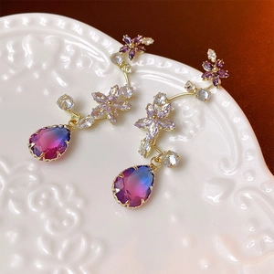 Close-up of gold floral earrings with crystal teardrop charms on a decorative white plate