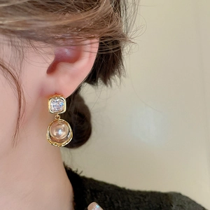 Close-up of gold-plated earrings featuring zircon studs and champagne pearls on a model