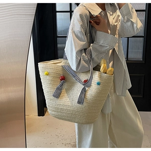 Close-up of beige woven tote bag with striped straps and colorful decorative pom-poms